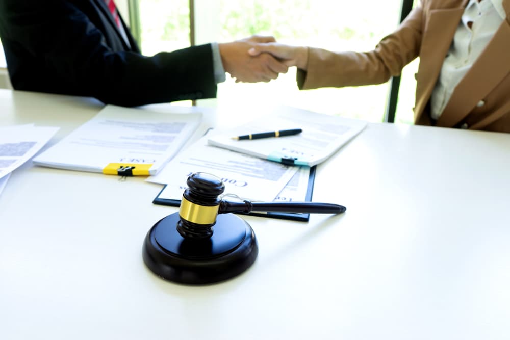 A lawyer or judge, holding a gavel and balance scale, shakes hands with a client or customer to discuss an arbitration agreement.